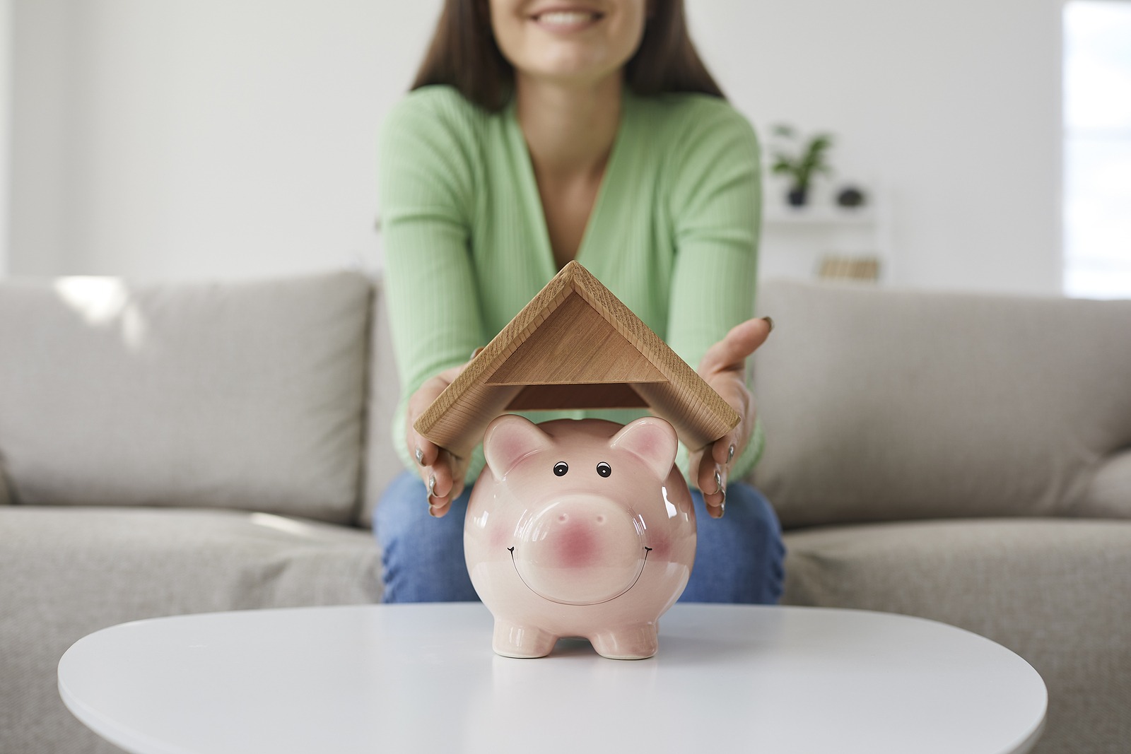 Happy woman who plans buying house or taking mortgage holding roof above piggy bank